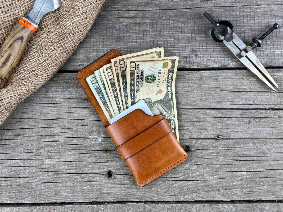 Minimalist genuine leather wallet with cash and tools on a rustic wooden surface.