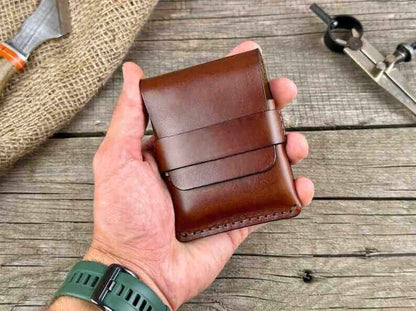 Hand holding a minimalist genuine leather wallet on a rustic wooden table.