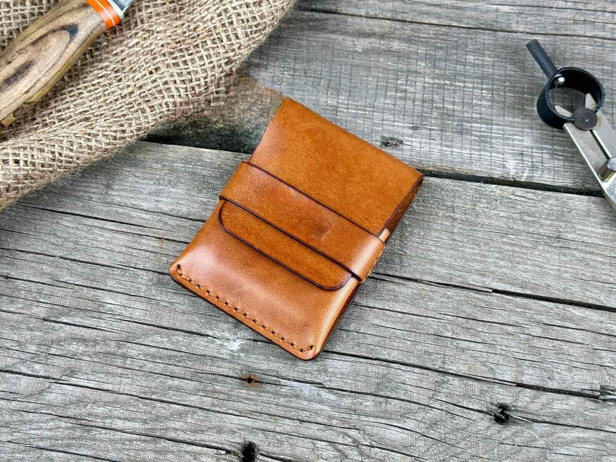 Minimalist genuine leather wallet displayed on rustic wooden surface with tools in background.