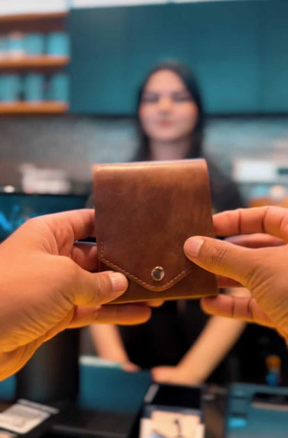compact leather wallet with pen: Pathfinder held in hands, with a blurred person behind in a cafe setting.